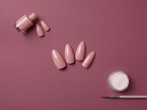 Gel polish bottle, nude press-on nails, and acrylic powder with a brush on a mauve background