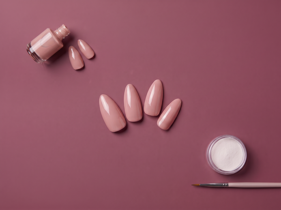 Gel polish bottle, nude press-on nails, and acrylic powder with a brush on a mauve background