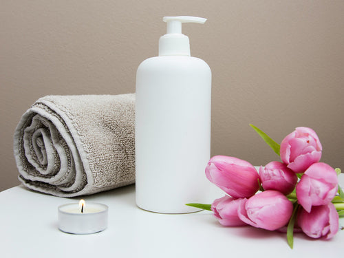 Pink tulips beside a rolled towel and a pump bottle in a calm, spa-like setting