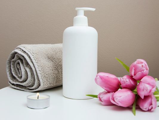Pink tulips beside a rolled towel and a pump bottle in a calm, spa-like setting