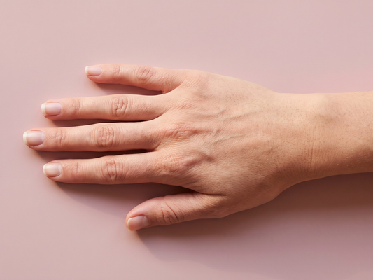 Relaxed bare hand with short natural nails resting on a blush pink surface