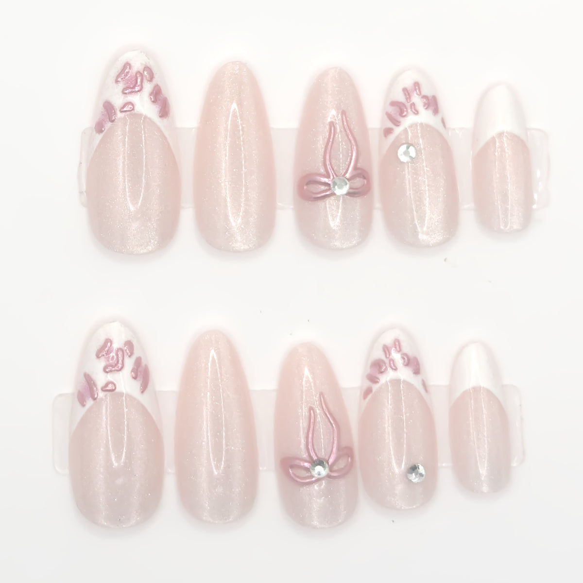 Close-up of blush almond press-ons with pink bows, white French tips, and a gemstone