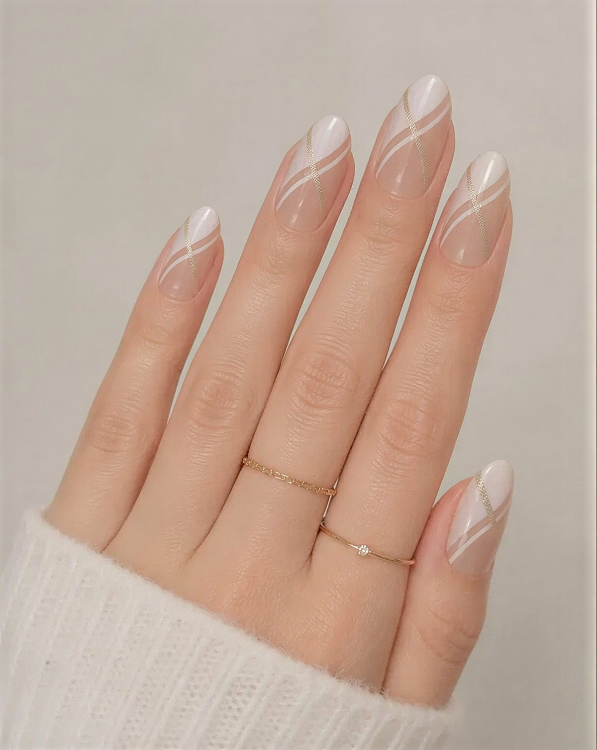 Hand with long, manicured nails and a gold ring on a neutral background
