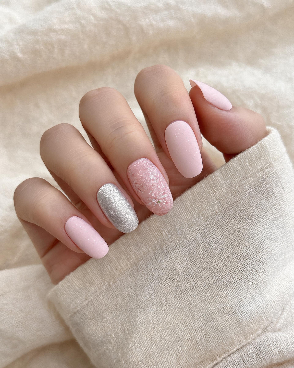Close-up of a hand with pink and silver nail polish on a beige fabric background