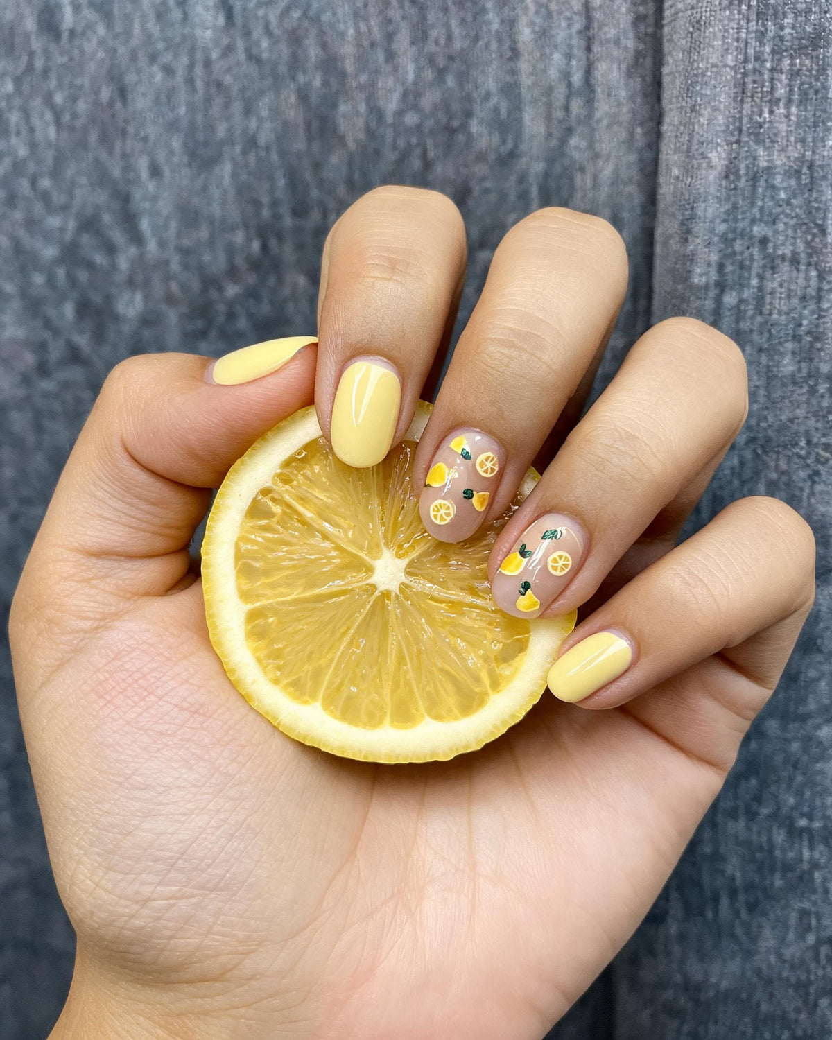 Hand with yellow nail polish holding a lemon slice against a gray background
