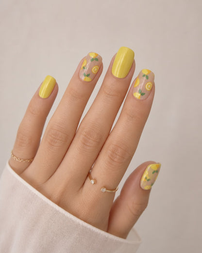 Hand with yellow nail polish and floral designs on a neutral background