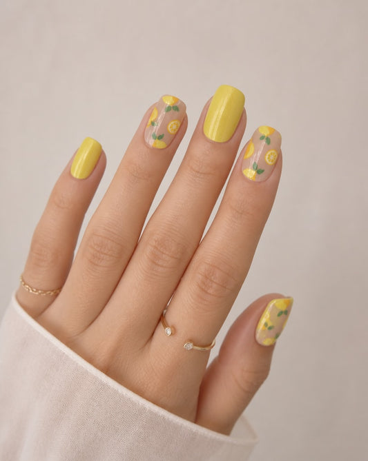 Hand with yellow nail polish and floral designs on a neutral background