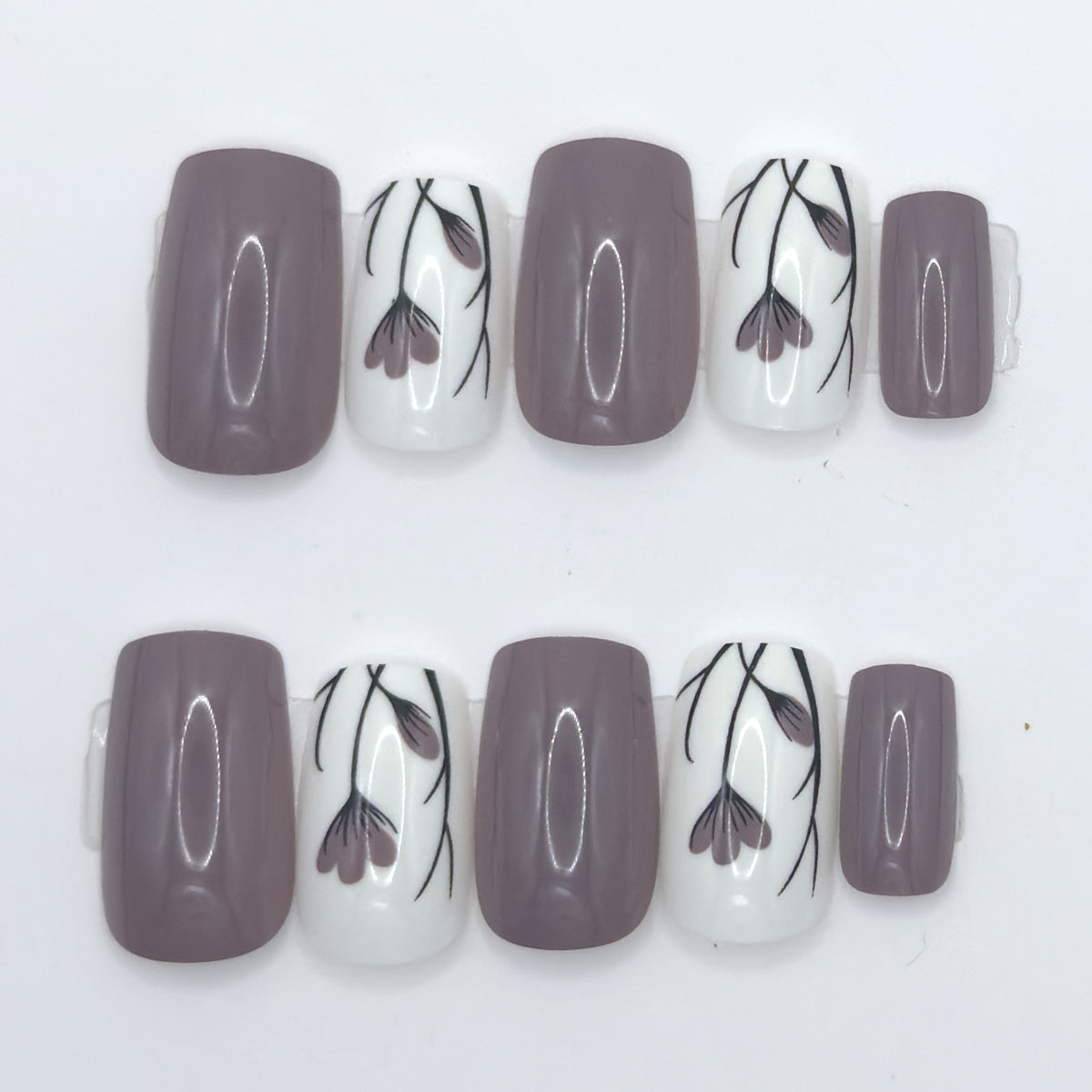 10 press-ons in two rows: glossy taupe nails and white nails with black and mauve tulip line art