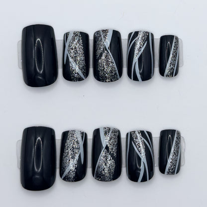 10 glossy black press-ons in two rows, some with silver glitter streaks and white swirl lines