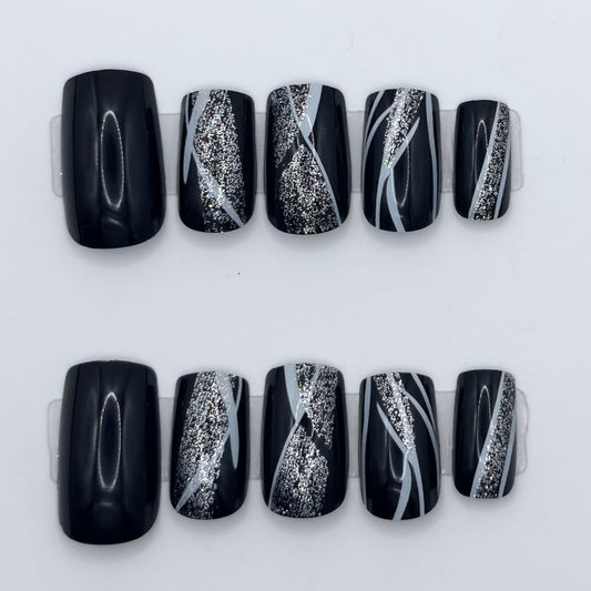 10 glossy black press-ons in two rows, some with silver glitter streaks and white swirl lines