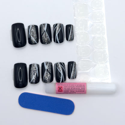 Glossy black nails beside a sheet of adhesive tabs, nail glue, and a nail file