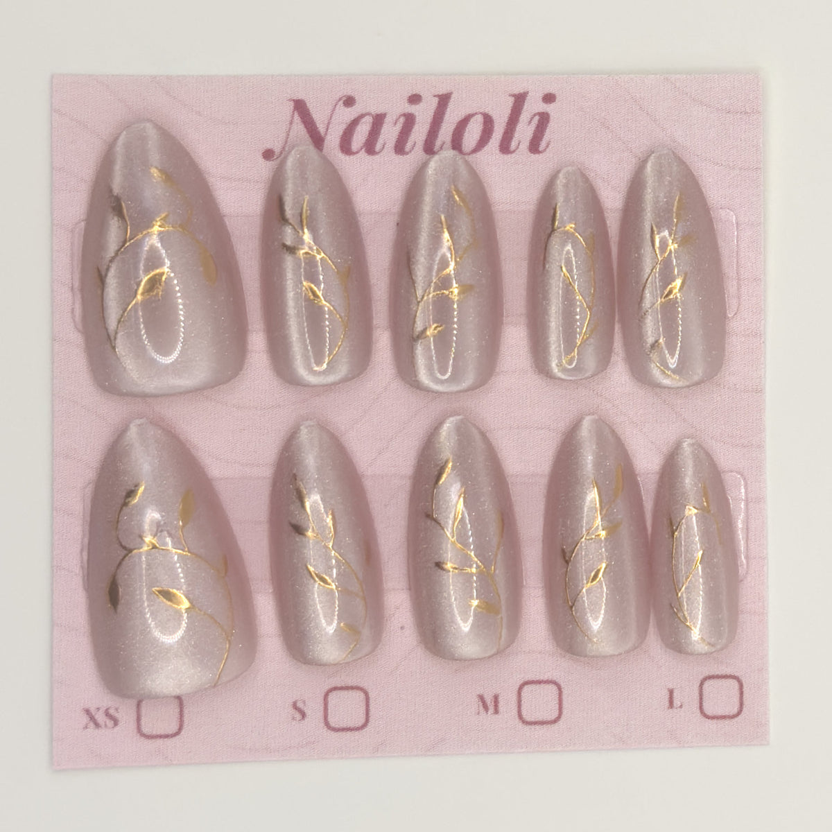 Set of gray nail extensions with gold designs on a pink 'Nailoli' branded card.