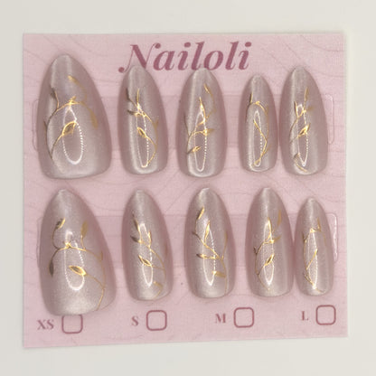 Set of gray nail extensions with gold designs on a pink 'Nailoli' branded card.