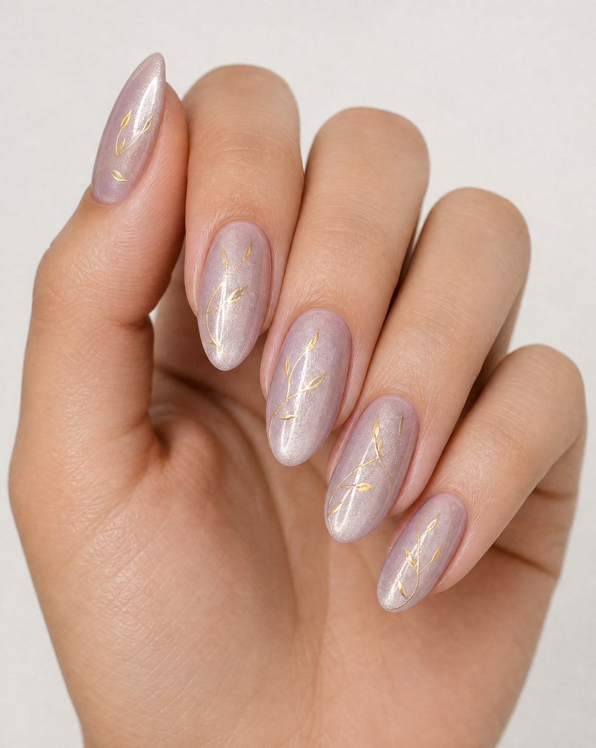 Hand with pink nails featuring gold leaf designs on a light background