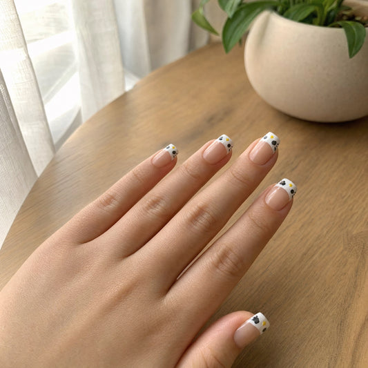 Hand on a wooden table wearing sheer blush coffin press-ons with white cat face and cowprint tips