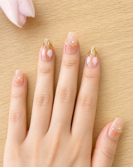 Close-up of a hand on a light oak table wearing short sheer peach coffin press-ons with 3D tulips and beaded pearl flowers