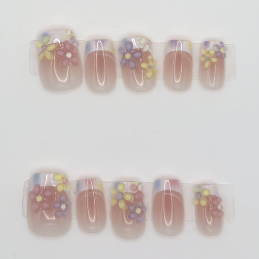 10 sheer pink press-ons in two rows with iridescent tips and purple, yellow, and red 3D flowers