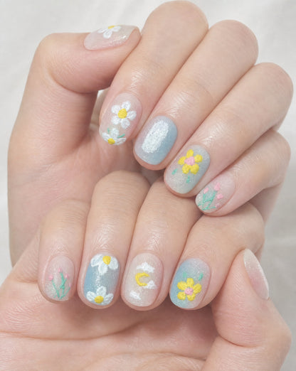 Hand wearing milky sheer square press-ons with textured daisies, tulips, and a yellow flower