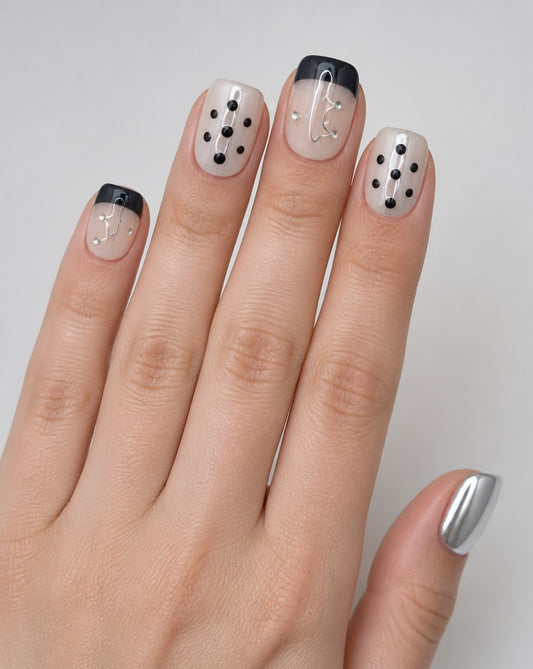 Hand wearing sheer nude square press-ons with black French tips, black dots, and tiny gemstones