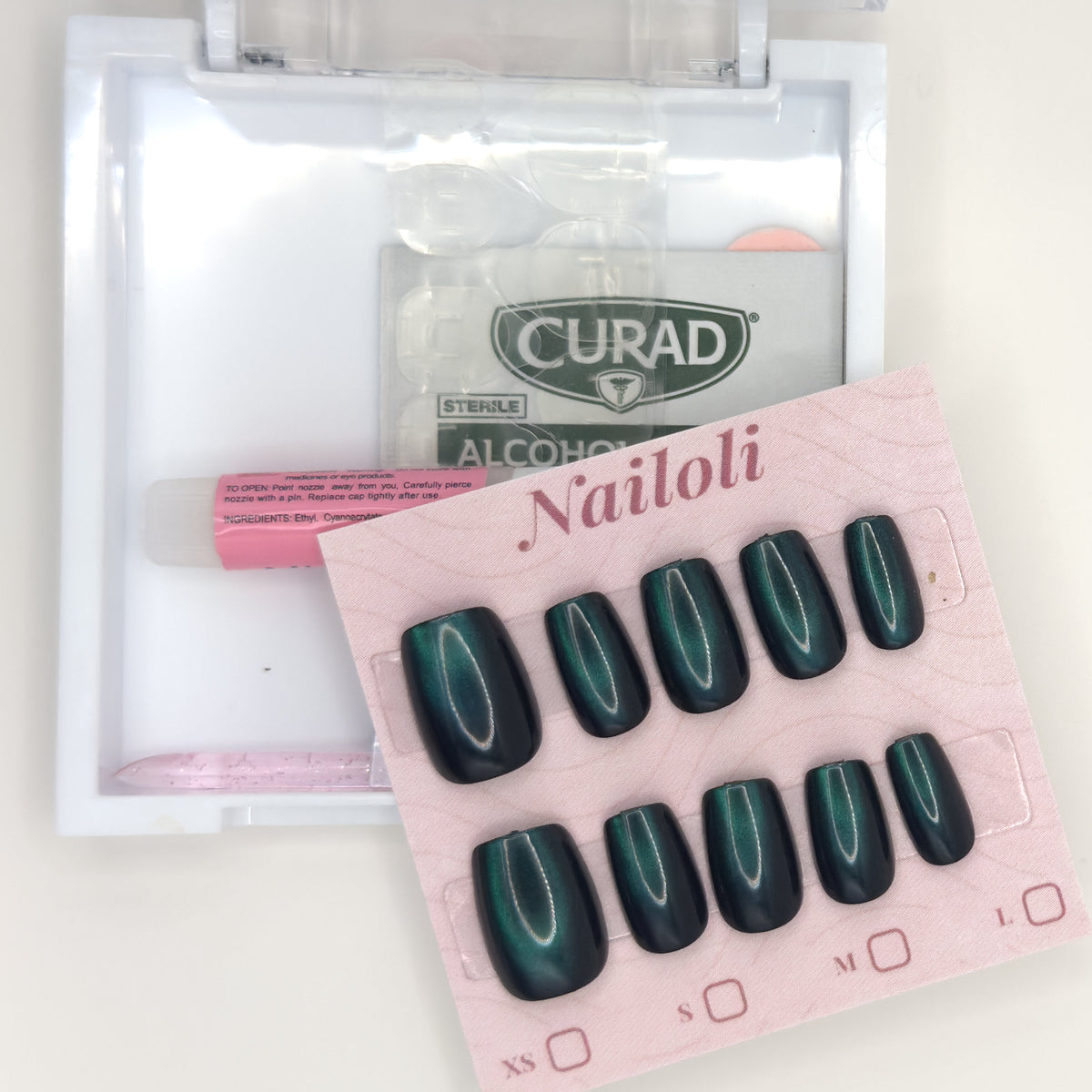Emerald cat eye set on its backing card beside the open kit with nail glue and alcohol prep pad