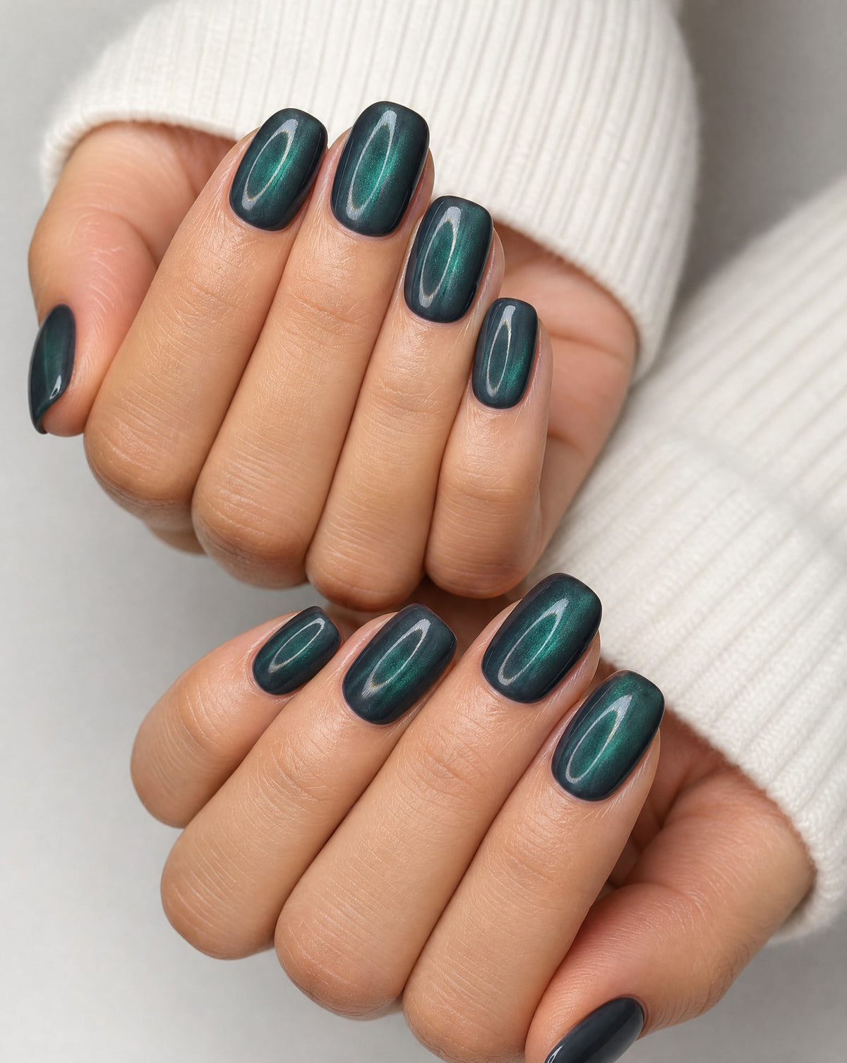 Hands in a white sweater wearing emerald cat eye square press-ons with a magnetic chrome shimmer