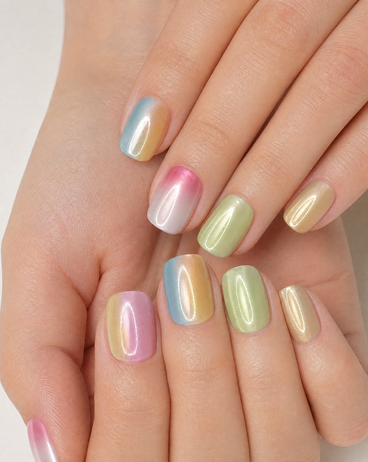 Hand wearing pastel chrome square press-ons in blue, pink, lime, and gold ombre shades