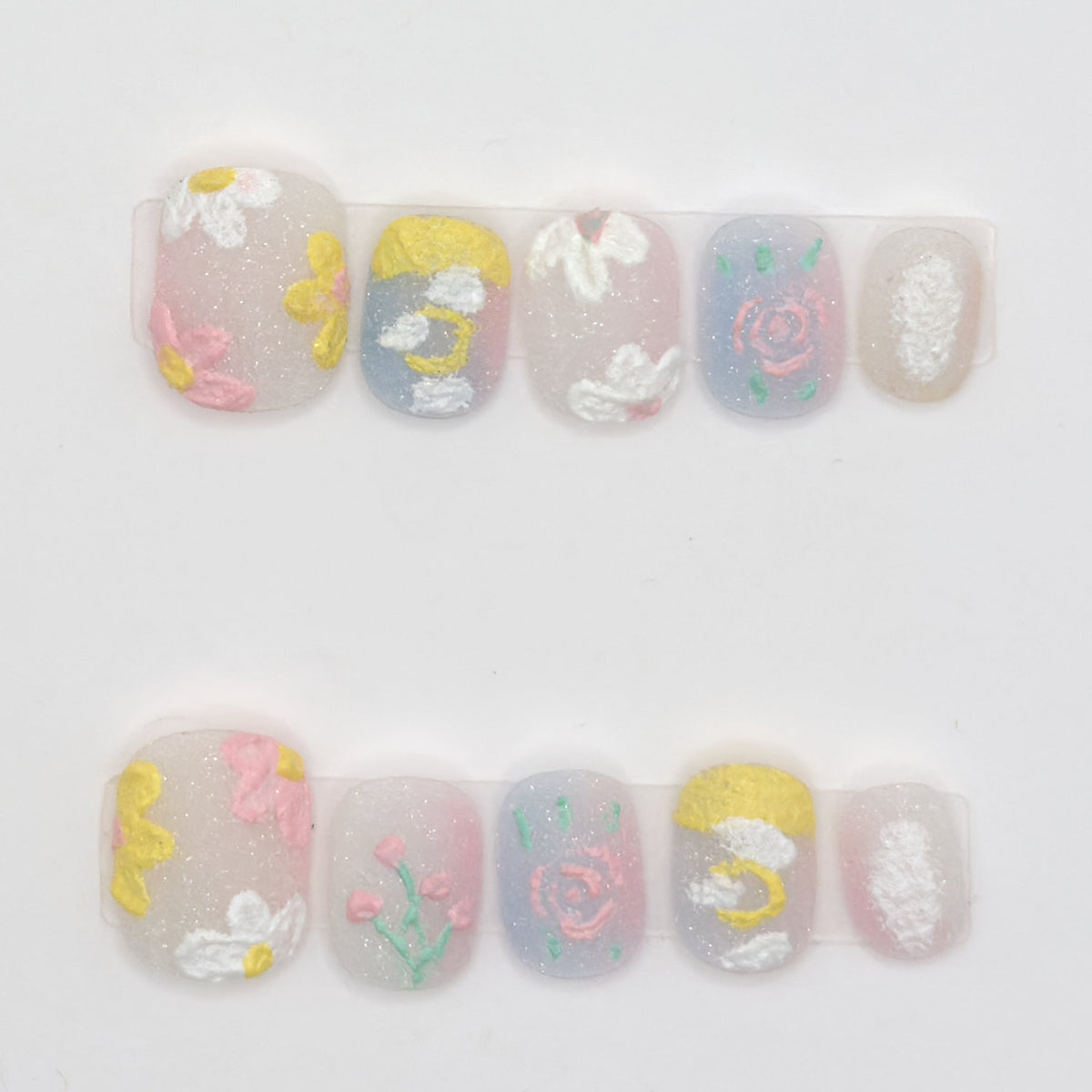 10 milky pastel press-ons in two rows with textured white daisies, pink roses, a moon, and sparkle