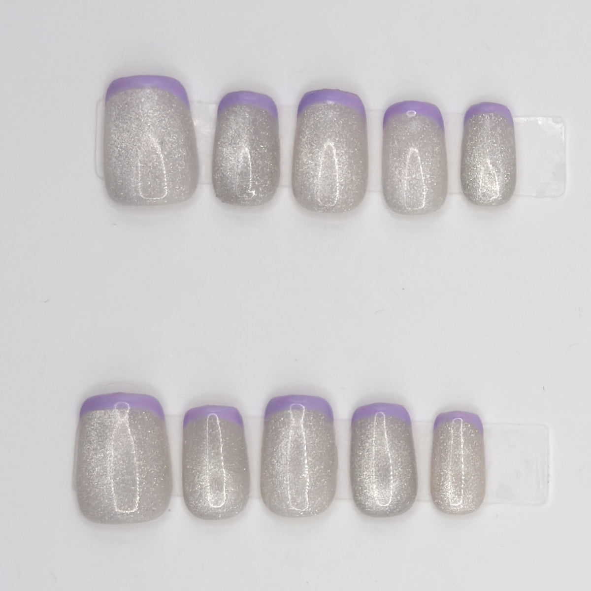 Close-up of 10 silver holographic square press-ons in two rows with thin lavender French tips
