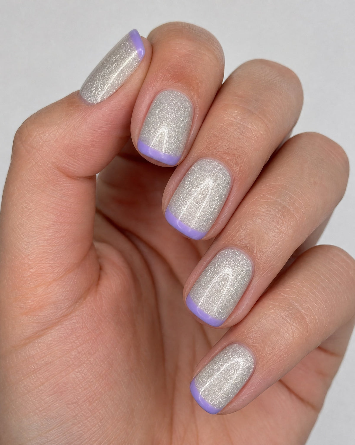 Hand wearing silver holographic square press-ons with lavender French tips