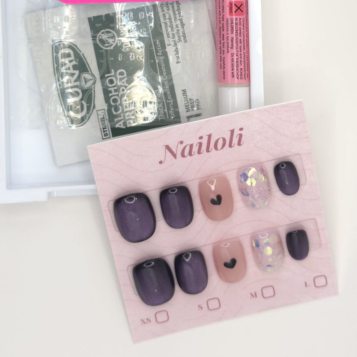 Velvet plum set on its backing card beside the open kit with alcohol prep pad and nail glue