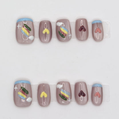 10 taupe press-ons in two rows with yellow, burgundy, and coral hearts, blue tips, and rainbow art