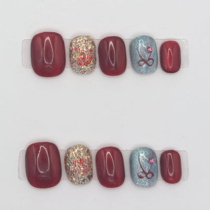 10 burgundy press-ons in two rows with gold glitter and a pale blue nail with a red bow and gemstone