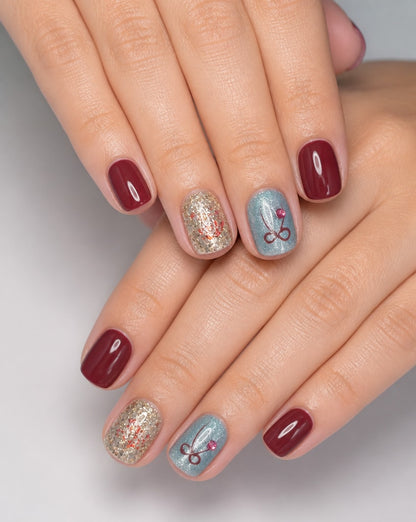 Hands wearing burgundy square press-on nails with gold glitter and pale blue bow accent nails
