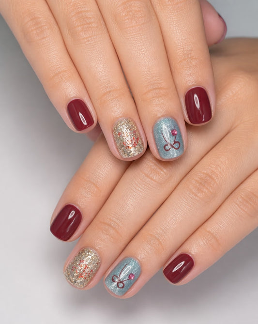 Hands wearing burgundy square press-on nails with gold glitter and pale blue bow accent nails