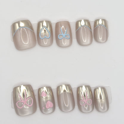 Close-up of 10 champagne chrome press-ons in two rows with blue and pink heart and bow line art
