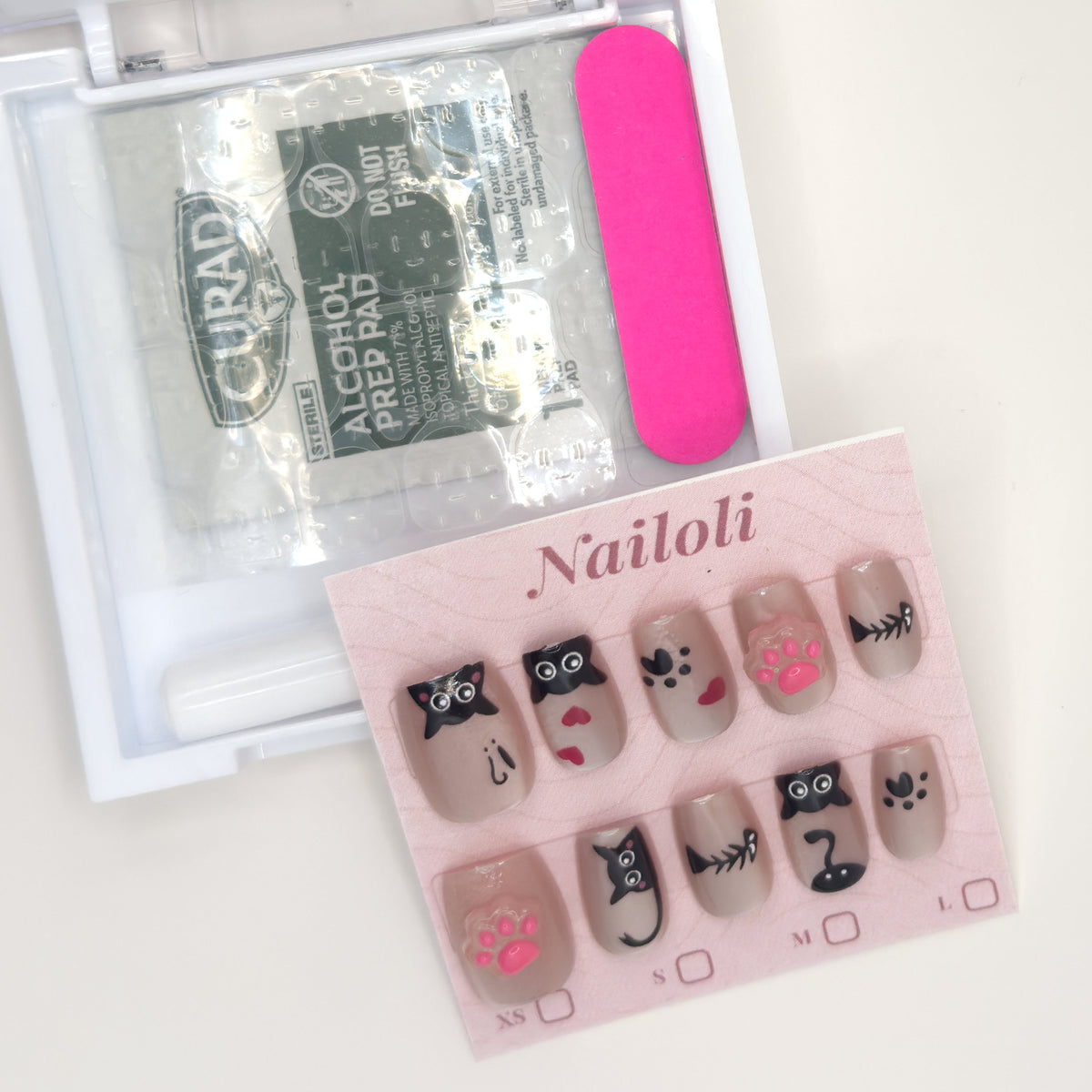 Kawaii cat set on its backing card beside the open kit with alcohol prep pad and nail file