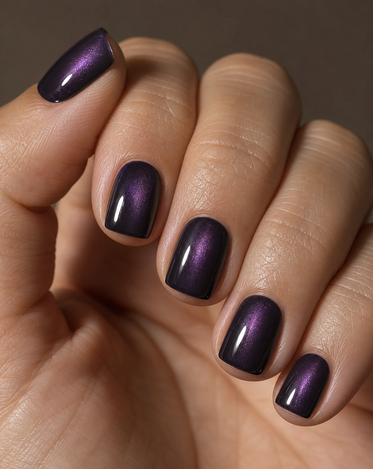 Close-up of a relaxed hand wearing extra short blackberry square press-ons with a soft violet cat eye shimmer