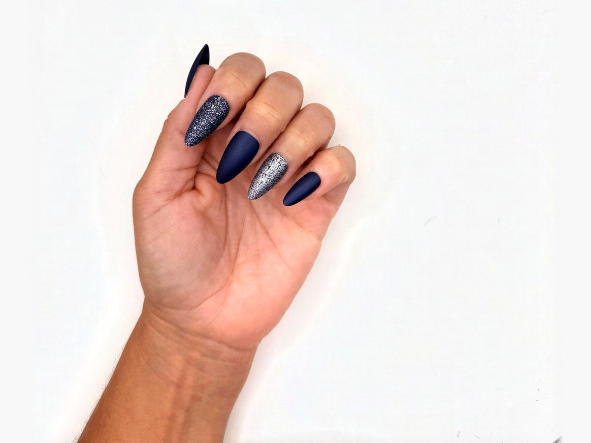 Hand curled toward the camera showing navy matte and glitter press-on nails