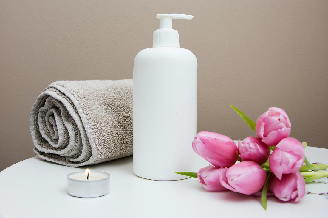 Pink tulips beside a rolled towel and a pump bottle in a calm, spa-like setting