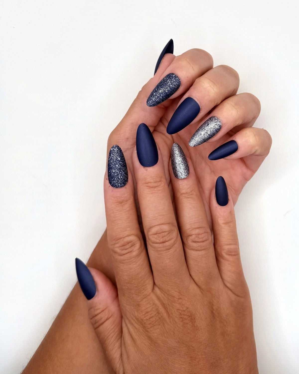 Hands posed together showing ten navy matte, glitter, and silver press-on nails