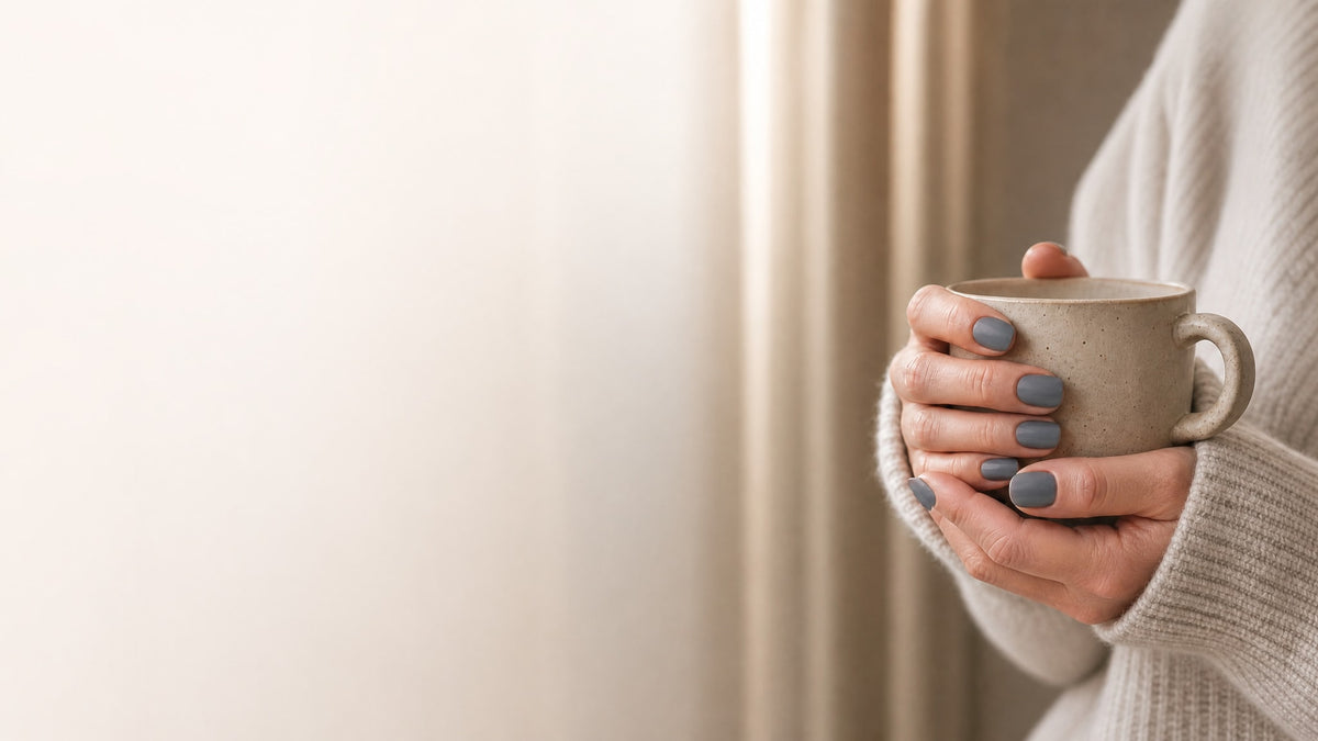 Hands with slate gray press-on nails holding a stone ceramic mug against a cream knit sweater