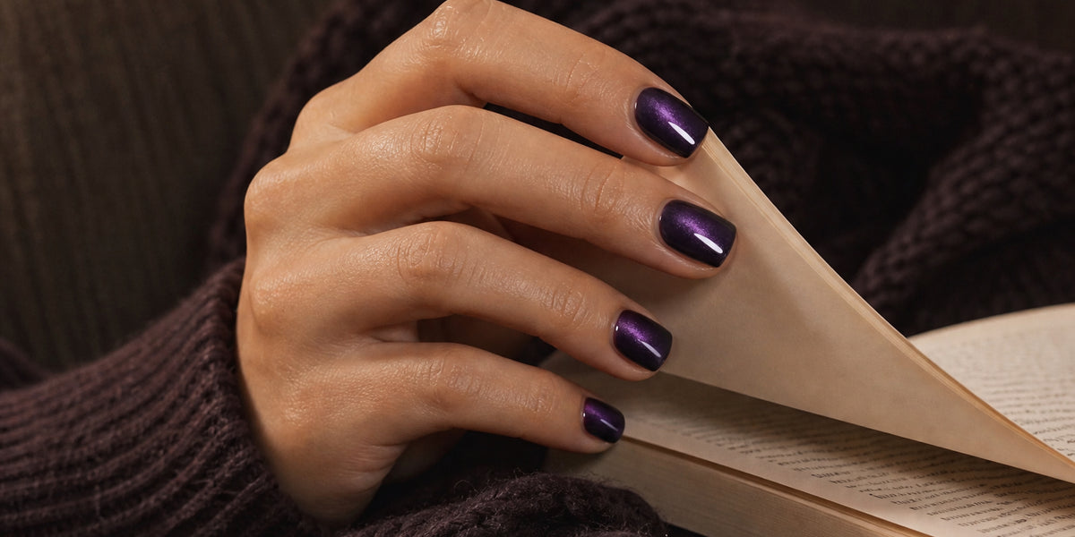 Hand with blackberry cat eye square press-on nails turning the page of a book on a cozy couch